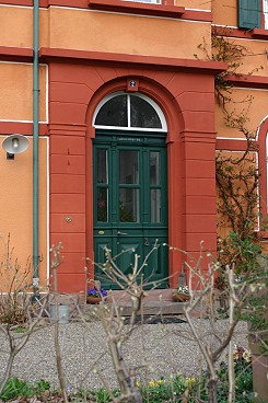 Die kr�ftigen Farbkontraste, rot f�r die W�nde, gr�n f�r die Holzbauteile, lenken trotz des dunklen Farbtons den Blick auf die Haust�r.